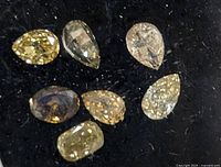 Seven loose natural fancy color diamonds on black fabric, showing variety in shapes and colors including yellow and light brown.
