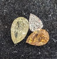 Three pear-shaped diamonds of yellow, white, and orange hues displayed on black background.