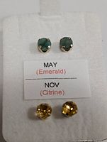 Front view of emerald and citrine stud earrings on white card with birthstone labels.