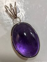 Close-up image of the oval cabochon amethyst pendant set in silver showing its color, silver bezel and triple bail.