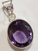 Close-up image of faceted deep purple amethyst pendant with silver setting and triangular bail with a circular accent.