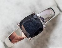 Close-up image of the ring showing cushion-cut blue sapphire gemstone on a polished silver band.