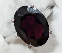 Front close-up of oval garnet gemstone in silver ring setting, showing the deep red color and faceted cut of the stone.