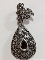 Close-up front view of silver pendant showing marcasite detailing and central pear-shaped garnet stone.