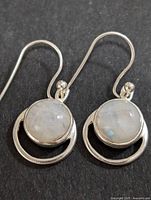 Close-up of pair of silver moonstone drop earrings on black background showing round moonstones and circular silver frame