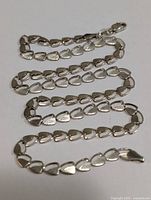 Silver necklace arranged in a wavy line showing heart-shaped links and lobster clasp.