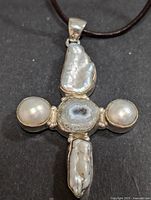Front view of the silver cross-shaped pendant showing two round pearls, geode center, and two baroque pearls with attached cord.