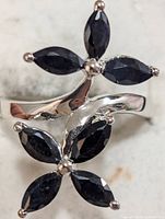 Clear close-up photo showing the silver ring with two flower-shaped clusters of four marquise-cut dark sapphire stones each, arranged on a twisted band.