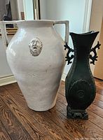 Overall view of the two urns side by side on a wood floor, showing size difference and details.