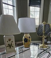 Three table lamps on glass table near window in daylight, showing all three lamp styles clearly.
