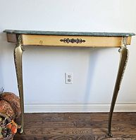 Full front view of the wall-mounted table showing green marble top, wooden frame with painted floral decorations, and two ornate brass legs.