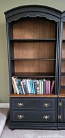Front view of black painted bookcase showing four shelves above two drawers with brass handles