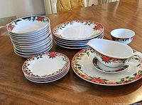 Collection of Christmas dinner plates, dessert plates, platter, gravy boat on table with bowls stacked to the side
