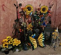 Wide shot of collection showing artificial flowers, metal butterfly, lantern, and other stakes arranged against pink backdrop on floor.