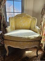 Front full view of chair showing soft yellow upholstery with white floral needlework and carved wooden frame.
