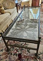 Full view of glass and metal coffee table showing the entire length and the ornamental metal design beneath the glass.