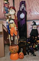 Group photo of Halloween and fall decor lot showing scarecrow figures, witch figure, pumpkin decorations, lanterns, wreath, and black cat figure in basement setting.