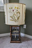 Front view of vintage lamp showing wooden base, glass front with candle inside, and fabric lampshade with botanical prints