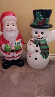 Photo showing two plastic light-up Christmas figures: Santa and Snowman standing on floor indoors.