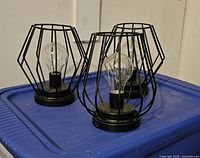 Three black metal cage patio lights with clear bulbs on blue surface.