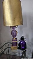 Full view of purple cut glass table lamp with gold-tone metal shade alongside small purple glass tea light lantern