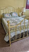 Full bed view showing brass bed frame with queen size floral quilt and two matching pillow shams.