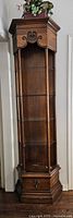 Full view of tall solid wood display unit with carved top, four glass shelves, slender wooden pillars, and bottom cupboard door.