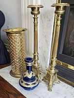 Full view showing two tall brass candlestick holders, brass umbrella stand, and blue glass vase with gold trim.