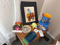 Overview shot of lot items on corner table, showing turtle dish, mugs, ashtrays, photo, calendar, and tin.