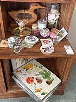 Photo of shelves with wood duck bank, brass candleholder with glass candle cup, various candles, coasters with bird and floral designs, and glass bird figurines.