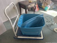Platform folding dolly with blue platform and white handle holding the large blue plastic storage container with lid.