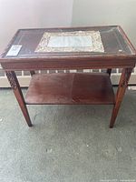 Front view of hand carved wood side table with glass top showing rectangular carved inset and wood shelf below