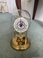 Full view of mantel clock with gold base, glass dome cover, and floral clock face.