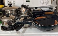 Photo showing assortment of Meyer cookware including pots with lids, Dutch oven, double boiler, frying pans with copper-colored interiors, and wok on stove top.