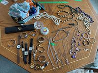 Overview of the lot showing jewelry spread on wooden table including necklaces, bracelets, watches, scarves, trinket box and ring holder