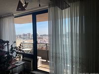 Curtains hanging on a balcony sliding glass door with cityscape view outside.