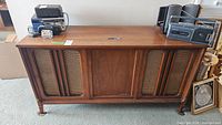 Front view of mid-century stereo cabinet showing wood finish, fabric speaker covers on sides, and central panel.
