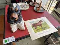 Spaniel figurine with one horse print on red table, visible details of figurine and print size