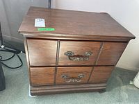 Wooden end table showing front and side view with two drawers, metal handles, and surface wear.