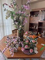 Tall brass vase with multi-colored faux flowers and botanical arrangement on table with other faux florals and artificial plants.