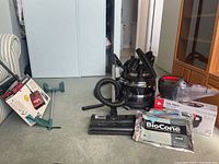 Full view of all items including the Filter Queen canister vacuum, attachments, extra vacuum bags, Dirt Devil cordless hand vacuum and sweeper with their boxes, and a grabber tool.