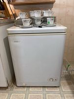 Front view of white Danby chest freezer with several tea cups and plates placed on top for scale reference.