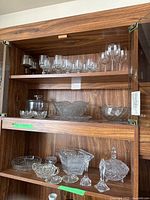 Full collection of glass and crystal items displayed on shelves including stemware, bowls, cheese keeper, fingertip tray, candy dishes, and candlesticks.