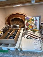 Photo of kitchen utensils including wooden cutting boards, woven baskets, metal cutlery, and a recipe book.