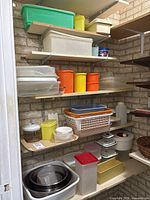 Several shelves holding plastic food storage containers in a variety of sizes and colors. Includes large and small bins, some opaque and some transparent containers, and vintage Tupperware canisters in bright orange and yellow.