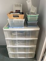 Full view of the large plastic storage container with four drawers topped with smaller containers and baskets including hangers and other plastic pieces.