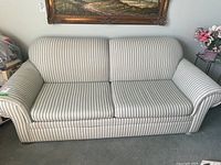 Front view of a three-seat striped upholstered couch showing rolled arms, striped fabric covering, and slight wear.