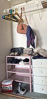 Pink 4-tier plastic shoe rack holding several shoes, small purses, and hangers on a white wall-mounted rack above.