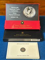 Top view of silver coin in red and black Royal Canadian Mint display box with certificate of authenticity below.