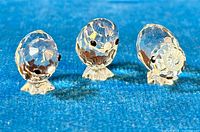 Front view of three Swarovski silver crystal bird figurines on blue fabric showing faceted bodies, heads, and black eyes.